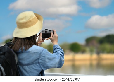 Rear view of woman traveller with backpack taking photo with digital camera while standing on a bridge over a canal - Shutterstock ID 2244725997