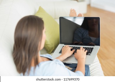 Rear View Of Woman Using Laptop On Sofa In The Living Room