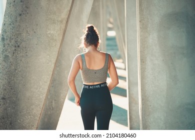 Rear view of a woman walking while training after doing a sprint run in an urban city outdoor view. Arab african woman on athletic wear and curly hair- - Powered by Shutterstock