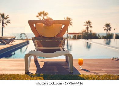 Rear view woman wear hat lying on deckchair near pool, put hands behind head relaxing, take sun bath, sea palm tree empty swimming pool scenery on background. Summer holidays, vacation, travel concept - Powered by Shutterstock