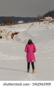 A Rear View Of Woman In A Winter Coat And Bonnet Walking On The Snowy Field