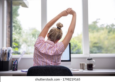 Rear View Of Woman Working From Home On Computer  In Home Office Stretching At Desk