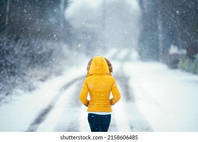 A Rear View Of A Woman In A Yellow Jacket Walking Outside Under The Snow In Cold Winter