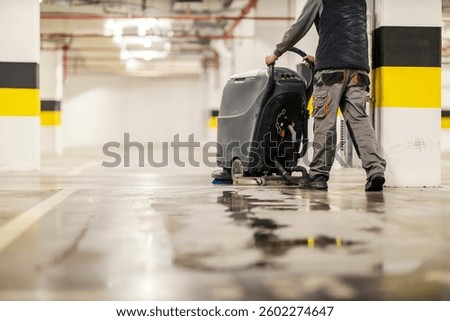 Rear view of worker using washing machine for cleaning garage floor.