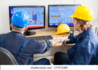 Rear View Of Workers In The Control Room, Looking At Computer Monitor