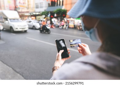 Rear View Of Young Adult Asian Woman Using Mobile Phone And Credit Card For Digital Wallet At Outdoor. People Using Electronic Banking Cashless For Travel Trip.