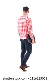 Rear View Of Young Adult Business Man Carrying Laptop Under Arm Walking And Looking Away. Full Body Isolated On White Background.