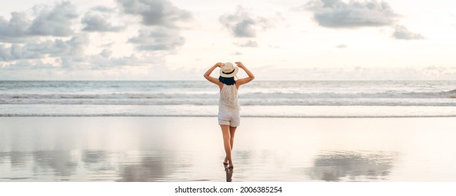 Rear view of young adult tourist asian woman walking relax on beach sand with beautiful dramatic sunset sky. Outdoor travel banner size background. - Shutterstock ID 2006385254