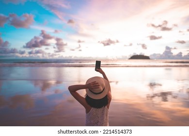 Rear View Of Young Adult Tourist Asian Woman Walking Relax On Beach Sand Using Smartphone For Take Photo. Outdoor Domestic Travel At Southeast Asia Andaman Ocean. Phuket, Thailand.