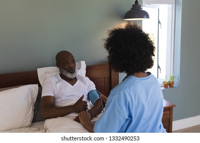 Rear view of young African American female doctor measuring blood pressure of senior African American man at home