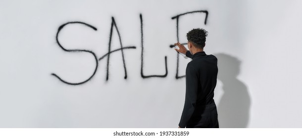 Rear View Of Young African American Man Writing Word Sale On Wall With Paint Sprayer, Panorama. Discount And Sale Concept