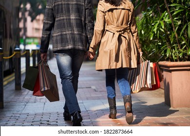 Hinteransicht des jungen asiatischen Ehepaares auf der Straße mit Einkaufstüten in Händen