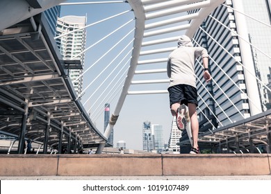 Rear view of Young athletic man jogging on city bridge, Sporty man running at morning with Bangkok urban scene background