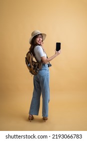 Rear View Of Young Attractive Asian Woman Traveler In Casual Clothes Wearing Straw Hat With Backpack And Camera Showing Mobile Phone For Presenting, Tourist Girl Having Cheerful Holiday Trip Concept