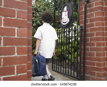 Rear View Of Young Boy With Backpack Entering School Gate