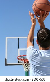 The rear view of a young boy shooting a basketball toward a hoop. Vertically framed shot.