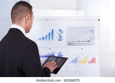 Rear view of young businessman analyzing graph on digital tablet in office - Powered by Shutterstock