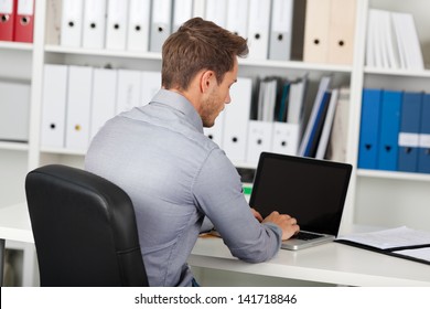 Rear View Of A Young Businessman Using Laptop At Office Desk