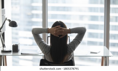 Rear view young businesswoman leaning back in comfortable chair, sitting in modern office, successful woman employee looking out window, planning future, visualizing, pondering project strategy - Powered by Shutterstock