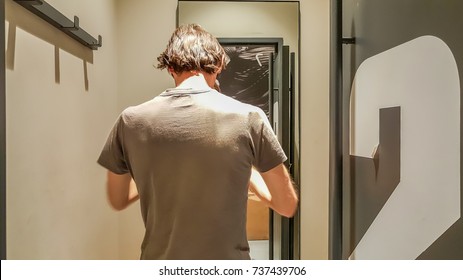 Rear View Of A Young Caucasian Handsome Man Standing In Front Of A Mirror In A Changing Room Of A Clothing Store