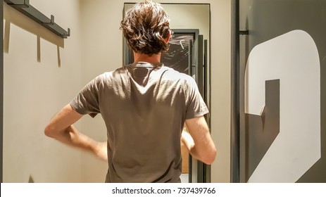 Rear View Of A Young Caucasian Handsome Man Standing In Front Of A Mirror In A Changing Room Of A Clothing Store