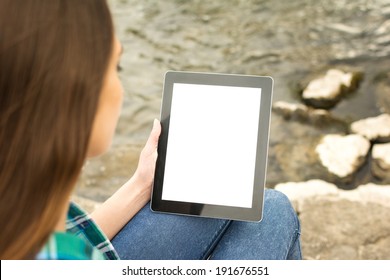 Rear view of young Caucasian teenage woman sitting by the river holding digital tablet with isolated blank screen.  - Powered by Shutterstock