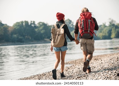 Rear view of young couple with backpacks walking hand in hand at the riverside - Powered by Shutterstock