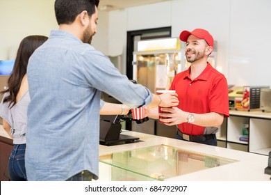 Rear View Of A Young Couple Getting Some Popcorn And Soda From A Worker At The Concession Stand In A Movie Theater