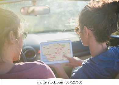 Rear View. Young Couple Lost On A Country Road Seeking Its Way On A Tablet. Backlit Shot With Flare