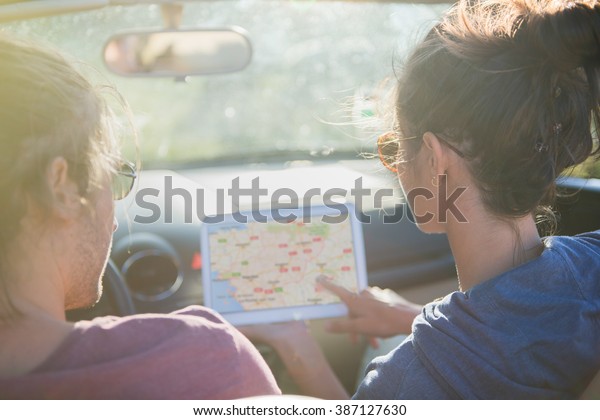 Rear view. Young couple\
lost on a country road seeking its way on a tablet. Backlit shot\
with flare