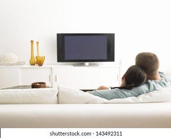 Rear view of young couple on sofa watching TV in living room