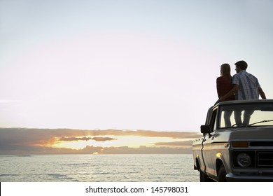 Rear view of young couple on pick-up truck parked in front of ocean enjoying sunset - Powered by Shutterstock