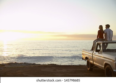 Rear view of young couple on pick-up truck parked in front of ocean enjoying sunset - Powered by Shutterstock