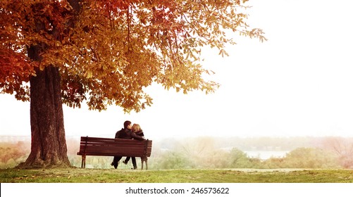 Rear View of Young Couple Sitting and Kissing on a Bench in the Beautiful Autumn Day . The man is embracing  her wife shoulder. Horizontal shot. - Powered by Shutterstock