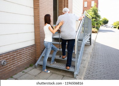 Rear View Of A Young Daughter Assisting Her Senior Father Climbing Staircase - Powered by Shutterstock