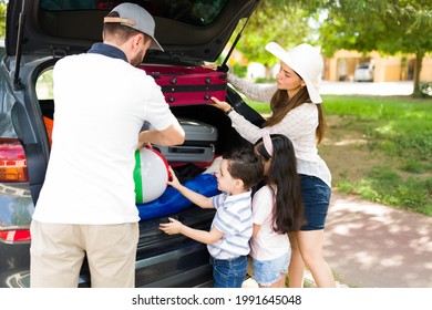 Rear View Of A Young Family Ready To Travel By Car. Cute Little Boy And Girl Packing Their Things With Mom And Dad To Go On A Vacation Trip