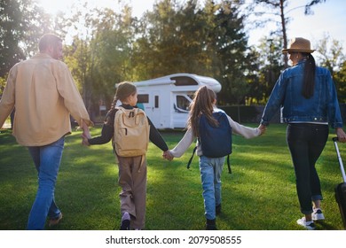 Rear View Of Young Family With Suitcases Going To Caravan Outdoors At Park.