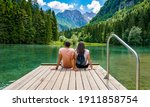 Rear view of young female sitting on wooden deck by beautiful lake in mountains  Green, spring, flower crown, outdoors  Zgornje Jezersko, Slovenia