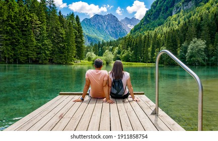 Rear view of young female sitting on wooden deck by beautiful lake in mountains  Green, spring, flower crown, outdoors  Zgornje Jezersko, Slovenia - Powered by Shutterstock