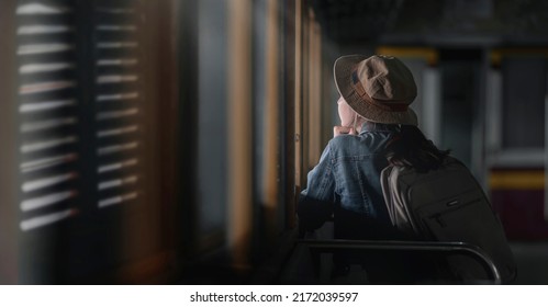 Rear View Of Young Female Traveler In Blue Jeans Sitting On The Train And Looking Away Outside Window.