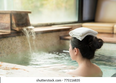 rear view of young girl enjoy the hot springs and put a towel on her head while water flows on the background.