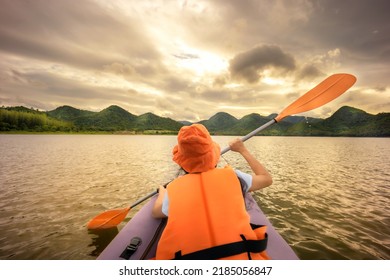 Rear view of young happy woman with life jacket safety paddling kayak on the river during sunset. Holiday Summer camp activity.