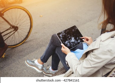 Rear view of young hipster girl is using portable touch pad for playing games, while is waiting car on a bus stop. Closeup image of stylish woman is holding digital tablet with copy space on screen - Powered by Shutterstock