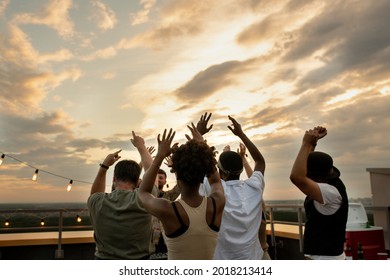 Rear View Of Young Intercultural Friends Enjoying Outdoor Party On Top Of Roof