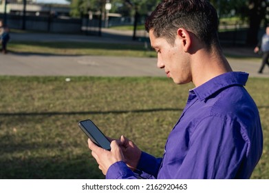 Rear View Young Latin Caucasian Argentinian Man, Outdoors In The Park, Checking The Mobile And Looking At The Phone Screen, Technology Concept.