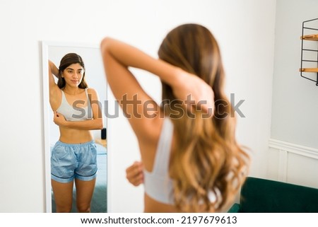 Rear view of a young latin woman doing self exploration or exam in the mirror to prevent breast cancer 