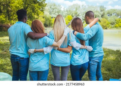 Rear View Of Young Male And Female Volunteers At Park. Environmentalist Are Walking With Arms Around. They Are In Blue T-shirts.