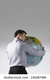 Rear View Of A Young Man With Arms Around Big Globe Against Gray Background