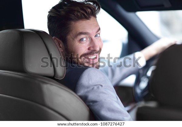 rear\
view, young man driving his car, looking at\
camera