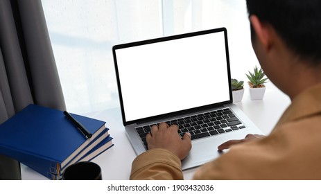 Rear view of young man freelance sitting at comfortable workplace and using laptop computer.